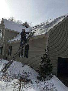 A man on a ladder cleaning the roof of his house.