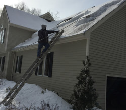 A man on a ladder cleaning the roof of his house.