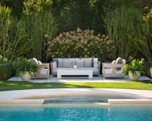 A pool with a white couch and chairs next to some bushes