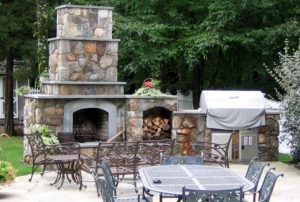 A patio with tables and chairs, a fireplace and trees.