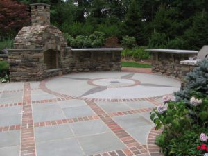 Stone patio with outdoor fireplace and greenery.