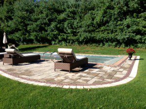 A patio with two lounge chairs and a pool.