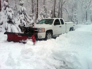 Pickup truck with snowplow in snowy forest.